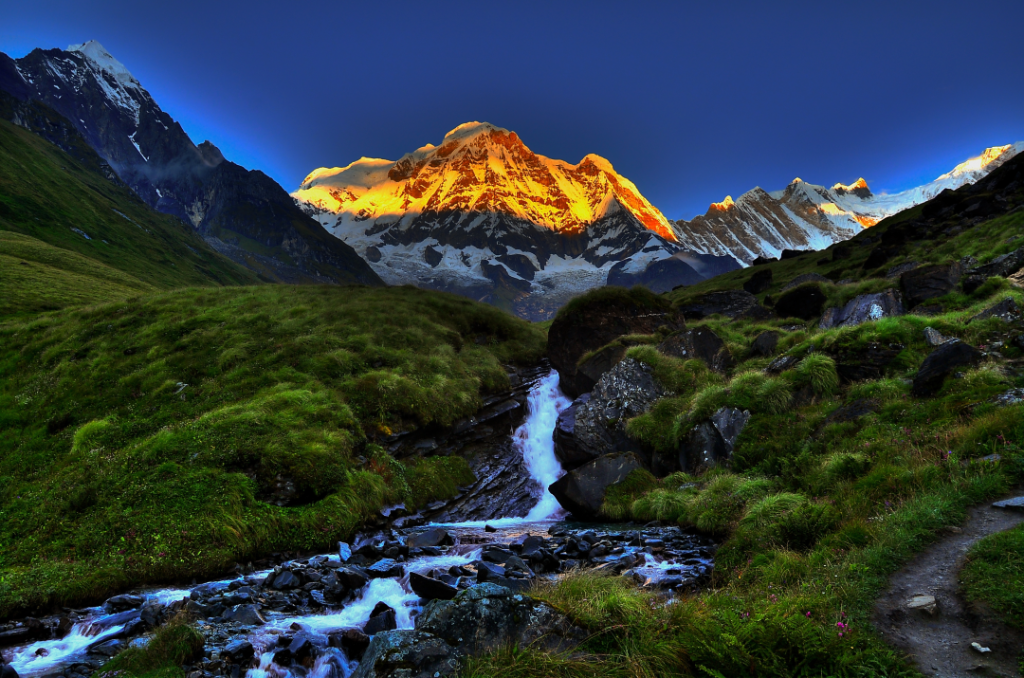 Scene of grassy banks, a stream and mountains in Nepal.